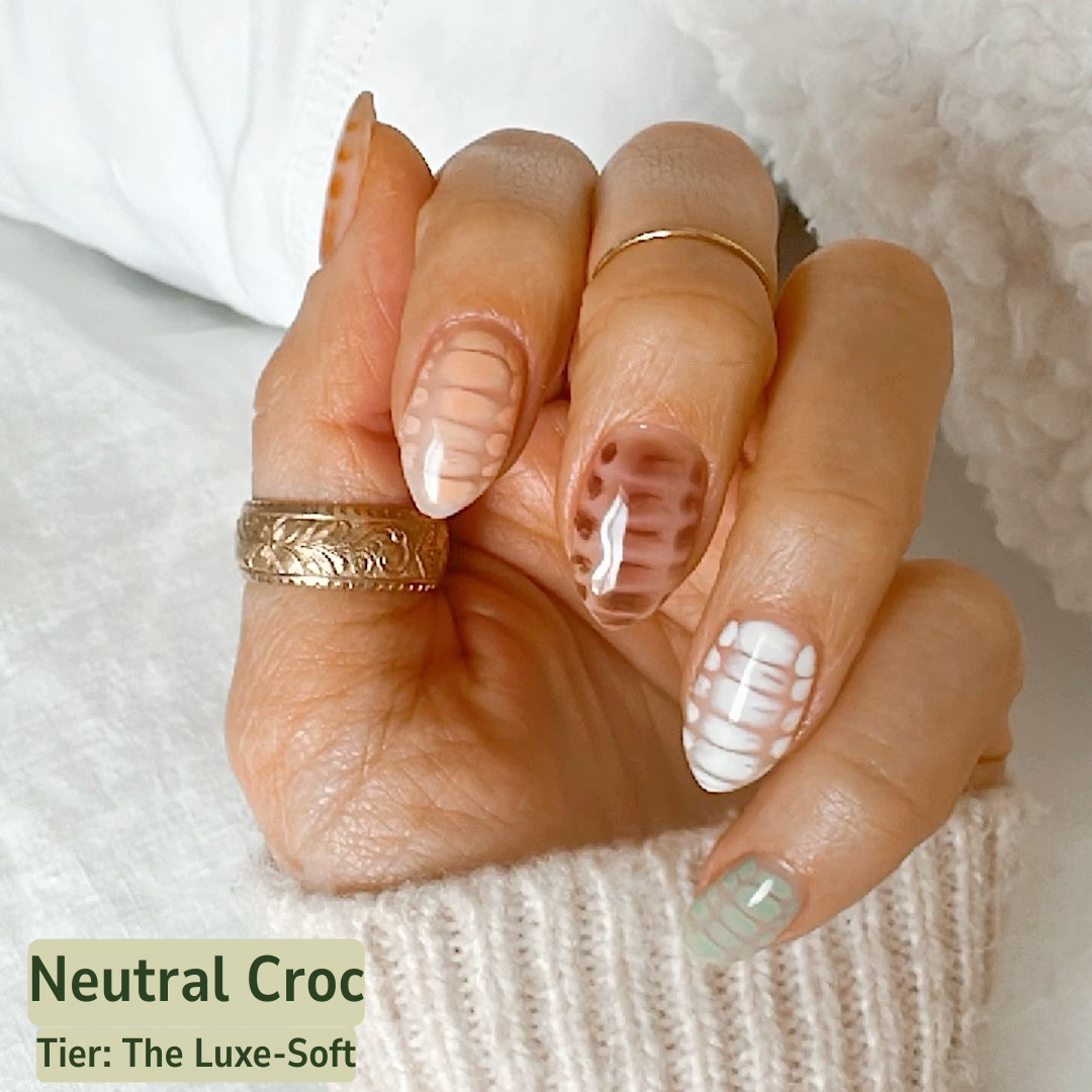 Close-up of a hand with neutral nail color and gold rings on a soft white background